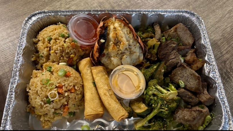 A takeout container with fried rice, lobster tail, egg rolls, beef, and broccoli.