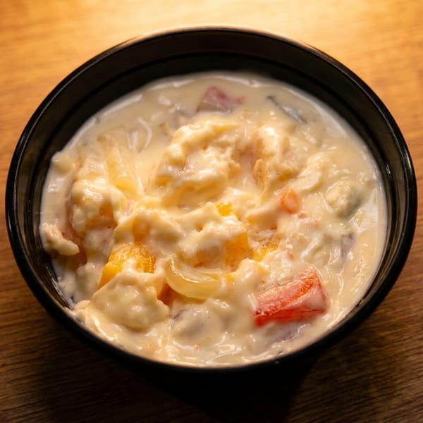 A black bowl filled with creamy fruit salad, featuring peaches, pineapple, and red fruit pieces.